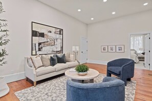 A cozy living room featuring a stylish setup with a large flat-screen TV mounted above a modern fireplace. A plush, inviting couch occupies the center, adorned with soft throw pillows. A sleek center table sits in front, adding a touch of elegance to