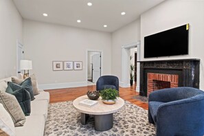 A cozy living room featuring a stylish setup with a large flat-screen TV mounted above a modern fireplace. A plush, inviting couch occupies the center, adorned with soft throw pillows. A sleek center table sits in front, adding a touch of elegance to