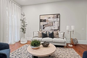 A cozy living room featuring a stylish setup with a large flat-screen TV mounted above a modern fireplace. A plush, inviting couch occupies the center, adorned with soft throw pillows. A sleek center table sits in front, adding a touch of elegance to