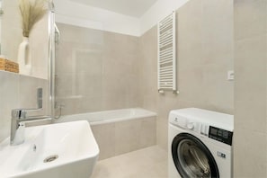 A functional bathroom with beige tiles, a washing machine, and a white sink for a clean and practical design.

