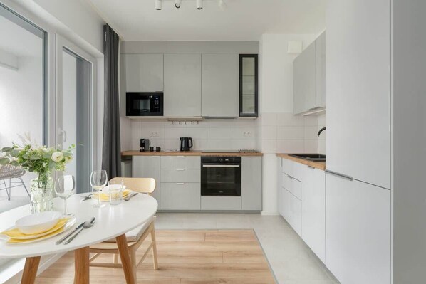 A compact kitchen with white cabinetry, integrated appliances, and a small dining table set for two with natural light flowing in.

