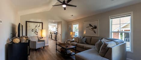 Spacious living room with smart TV, new couch, ceiling fan, and vaulted ceiling.
