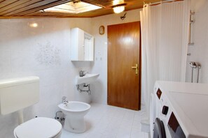The bathroom with shower, washing machine, toilet, bidet and sink