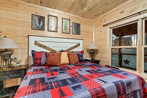 Relax in this rustic Smoky Mountain bedroom in Pigeon Forge, TN, featuring a king-size bed with a cozy quilt. Large windows bring in natural light, and rich wood tones create a peaceful retreat. Enjoy comfort in this cabin near Pigeon Forge attractions. Pet-friendly, hot tub cabin ideal for a romantic getaway.