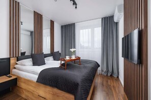 A sophisticated bedroom with a dark upholstered bed, wooden accent wall, and sheer curtains, maintaining a sleek, minimalist design.

