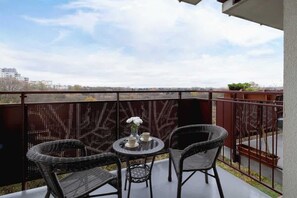 A balcony with a small round table and two wicker chairs, offering an outdoor relaxation spot with a view of the neighborhood.

