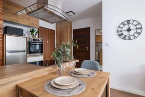 A cozy dining area with a wooden table set for two, complemented by a wall clock and modern pendant lighting for a warm, inviting atmosphere.

