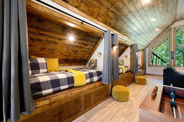 Wooden attic room with built-in beds, yellow accents, and large windows.
