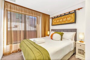 The second bedroom features a queen bed under beautiful wall art, warm side lamps and cosy throw pillows. Relax in soft sunshine flowing through curtains and feel at home with plenty of storage to unpack into. 