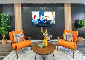 Vibrant eclectic-bohemian living room featuring a cozy seating area, colorful decor, and a 65-inch TV with a soundbar for premium entertainment