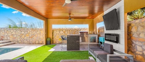 Fully equipped backyard living space: kitchen, propane grill, sink, refrigerator, TV and fireplace