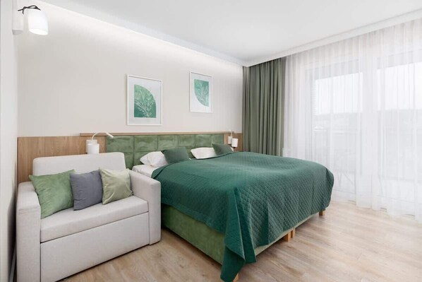 A cozy bedroom with a green bedspread, wooden headboard, and large windows.

