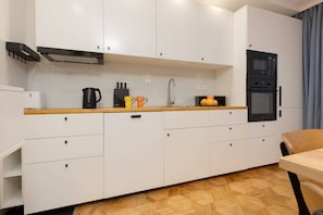 A minimalist kitchen with white cabinets, black appliances, and wooden flooring.