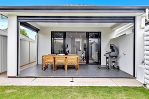 A spacious outdoor patio is complete with a BBQ and outdoor table setting for laidback afternoon cook-ups overlooking the private, grassy backyard.
