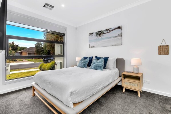 The light-filled primary bedroom features a queen-size bed with a side table and reading lamp, as well as a sleek, modern ensuite. 
