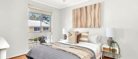 The light and airy first bedroom includes a ceiling fan and is thoughtfully appointed with a queen bed, side tables and reading lamps. 
