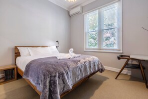 The light and airy primary bedroom is thoughtfully appointed with a queen-size bed, air-conditioning and a dedicated workspace.
