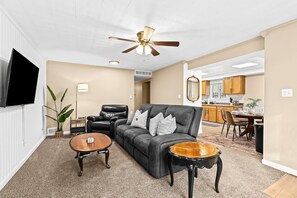 Spacious living area with comfortable leather seating, elegant lighting, and open-plan layout leading to a well-equipped kitchen, ideal for relaxation and socializing