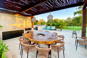 A shaded area with a natural wood dining table, BBQ, and sink area