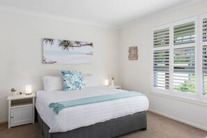 The spacious primary bedroom features a king-size bed with side tables and reading lamps and plantation shutters to filter light.
