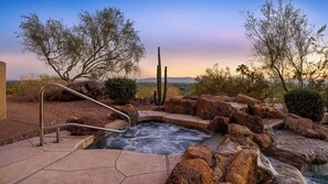 Relaxing spa with waterfall and panoramic sunset views in a rocky landscape.