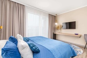 Another angle of the bedroom showing a wall-mounted TV and beige curtains.

