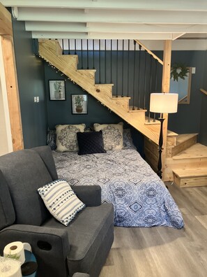 Queen bed tucked under stairs in main living area.