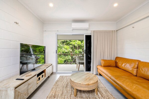A breezy, open-plan living area is complete with a cosy sofa to settle in with some TV, while glass doors opening to the balcony offer views of the tropical gardens. 
