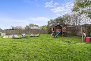Spacious backyard with sun loungers, play set and corn hole game