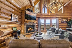 Unwind in the warm glow of this cozy living space with plush seating and a stone hearth. Rustic decor and a lofted ceiling add to the cabin’s charming atmosphere. 
