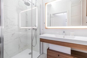 A sleek bathroom showcasing a glass-enclosed shower, marble-effect tiles, and wooden cabinetry.

