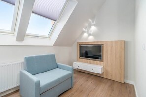 A bright living area with a light blue sofa, a white TV stand, and natural light streaming through skylight windows.

