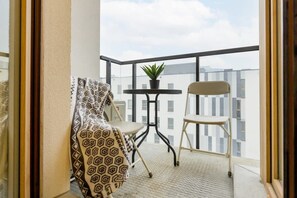 A balcony view with a small outdoor setup and surrounding cityscape visible in the background.