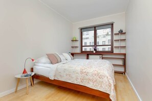 A cozy bedroom with a comfortable bed, wooden flooring, and a large window.