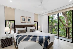 The primary bedroom boasts a king-size bed, a large ensuite with a bath, and direct balcony access with leafy views.
