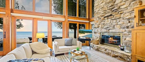 Expansive windows framing the picturesque beach and sky, the room bathes in natural light, enhancing the cozy yet modern decor. The space is designed for comfort and relaxation.