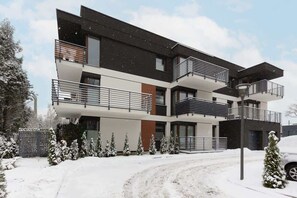 A winter exterior view of a modern residential building with snow-covered surroundings.