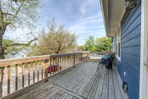 Spacious Wooden deck on the second floor of a home, featuring a natural wood railing and outdoor seating. It offers a view of trees, neighboring homes, and a quiet residential area