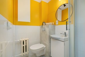 A modern bathroom with yellow accents, a round mirror, and white fixtures.