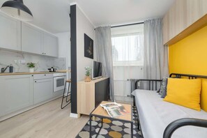 A modern studio with a functional layout – yellow accent wall, wooden built-in furniture, and a small sofa.