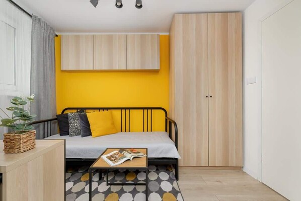 A modern studio with a functional layout – yellow accent wall, wooden built-in furniture, and a sofa.