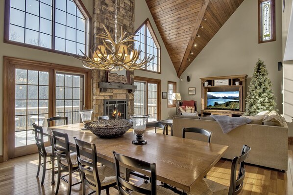 Dining/living with stone fireplace, wall of windows and high chalet ceilings