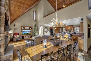 Dining/living with stone fireplace, wall of windows and high chalet ceilings