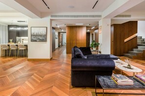 Another perspective of our inviting living space, capturing the seamless blend of the living room, sofa, kitchen, and a glimpse of a corridor. Experience the harmonious design of our Penthouse, where every corner reflects comfort, style, and a welcoming ambiance