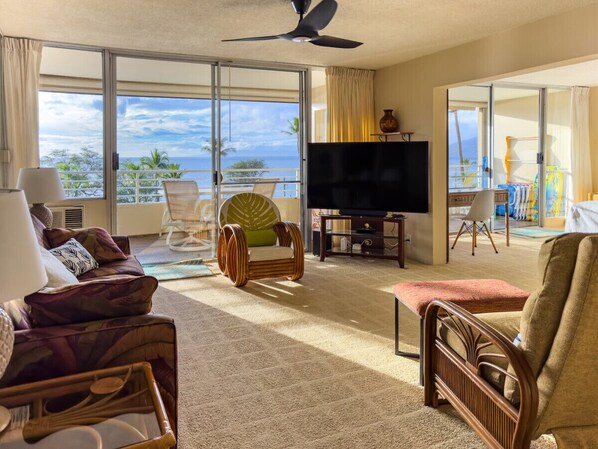 Living room & lanai with panoramic 180° ocean, sunset, West Maui Mountain, and Lanai Island views. 65" 4K  TV. The lanai sliders open up to create indoor-outdoor living Hawaii style.