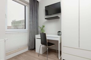 Another view of the bedroom, showing a wardrobe and a workspace with a desk and chair near a window.