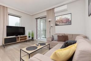 A modern living room with a large window, a cozy beige sofa, a coffee table, and a TV.