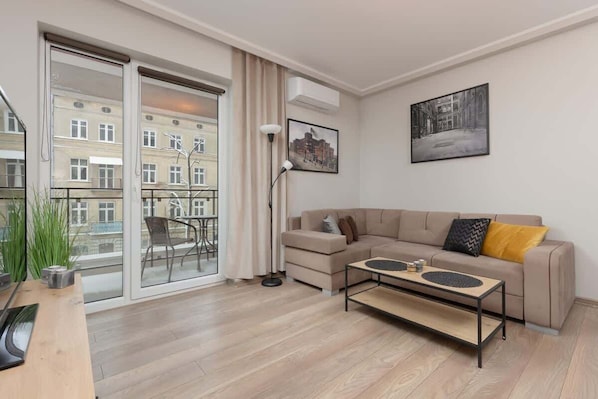 A modern living room with a large window, a cozy beige sofa, a coffee table, and a TV.