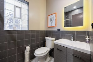 Bathroom with gray tile walls, a white sink and toilet, a large mirror, and a block glass window.