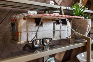 Silver model camper van with a red and white awning, a potted plant, and a decorative head on a shelf.